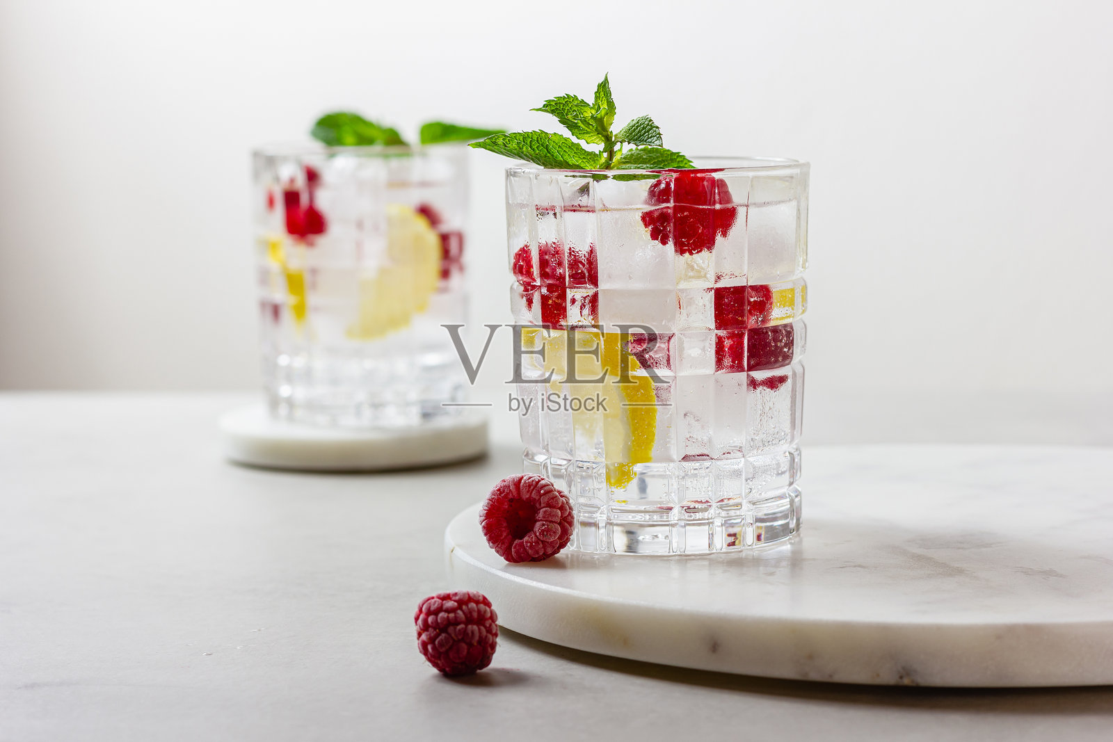 浅色背景下，玻璃杯中盛有带冰块的覆盆子鸡尾酒照片摄影图片