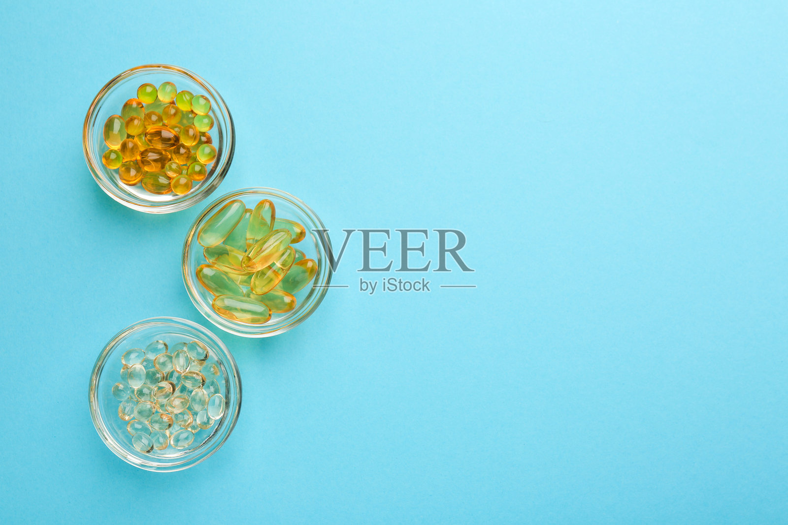 不同维生素胶囊盛放在碗中，背景为浅蓝色，俯视角度。留有文字空间。照片摄影图片