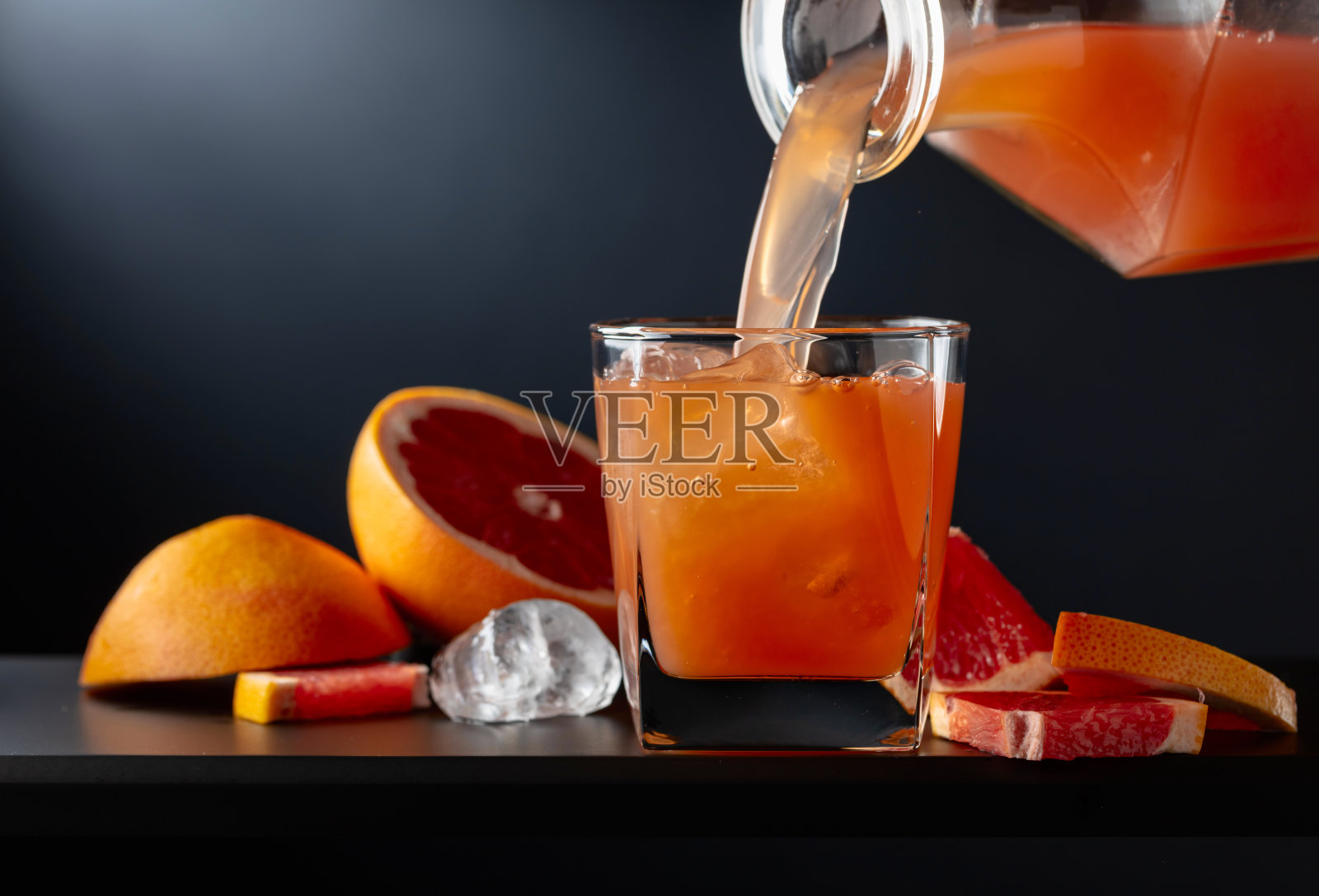 黑色背景上放着一杯加冰的西柚汁。照片摄影图片