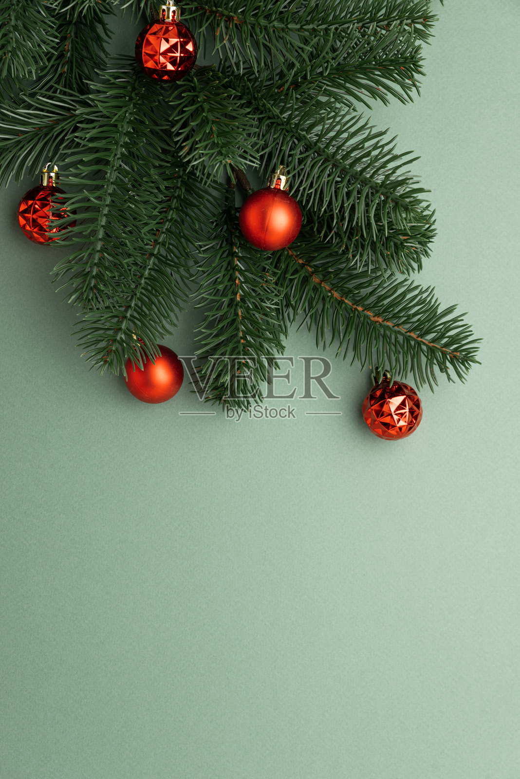 红色圣诞装饰品挂在松枝上，背景为柔和的绿色照片摄影图片