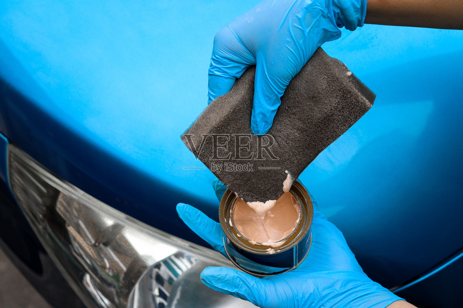 戴着蓝色手套用手给蓝色汽车引擎盖抛光打蜡照片摄影图片