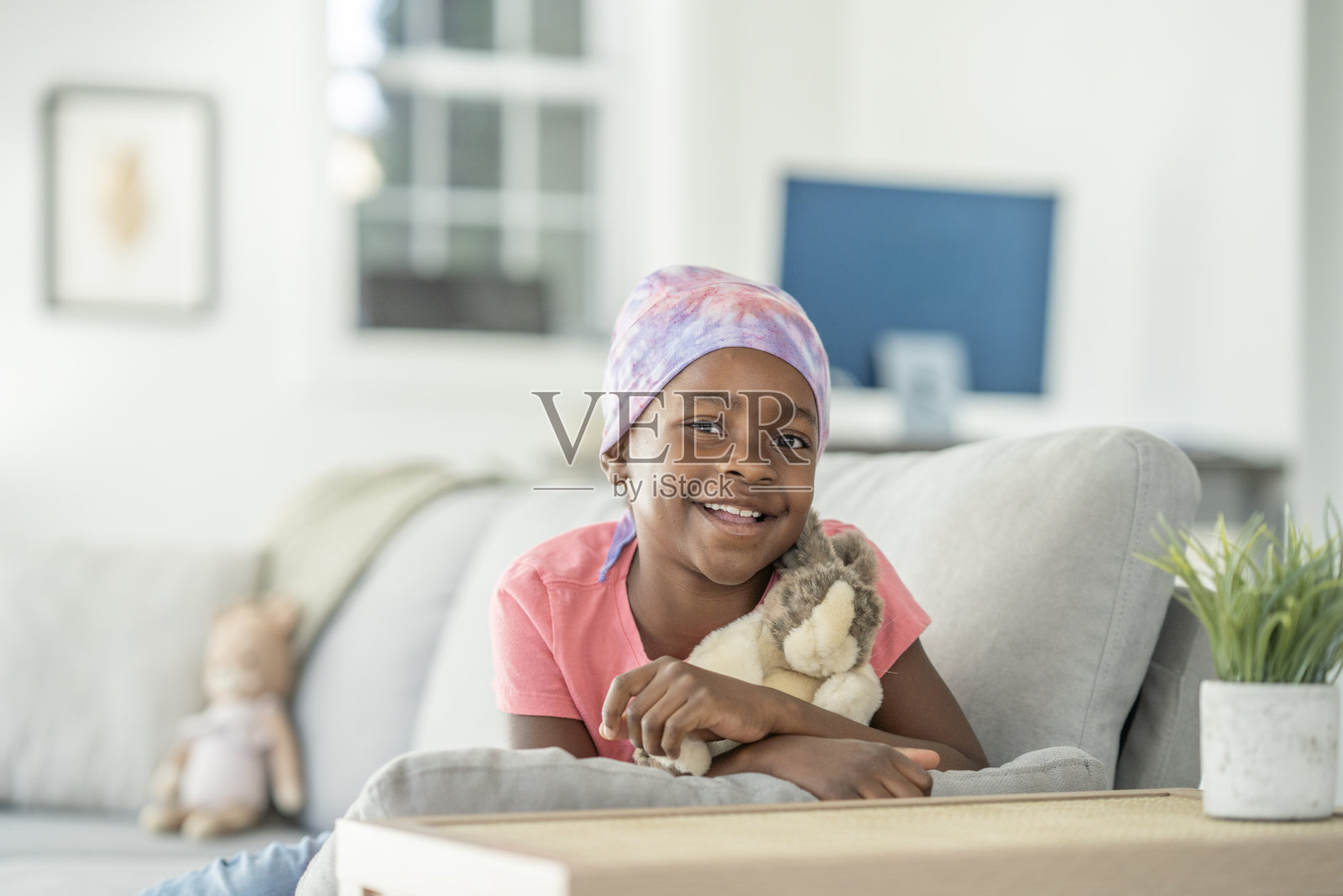 戴着头巾的快乐黑人女孩在舒适的客厅沙发上依偎着毛绒玩具照片摄影图片