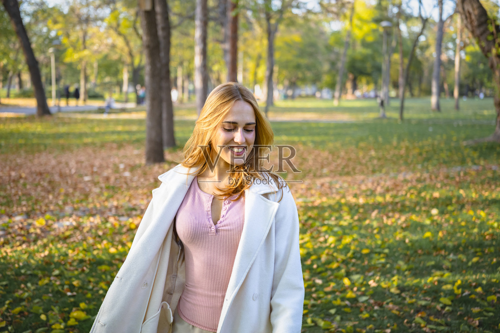 一位美丽的年轻女子在秋叶满地的公园里，享受着秋日的美好散步时光。照片摄影图片