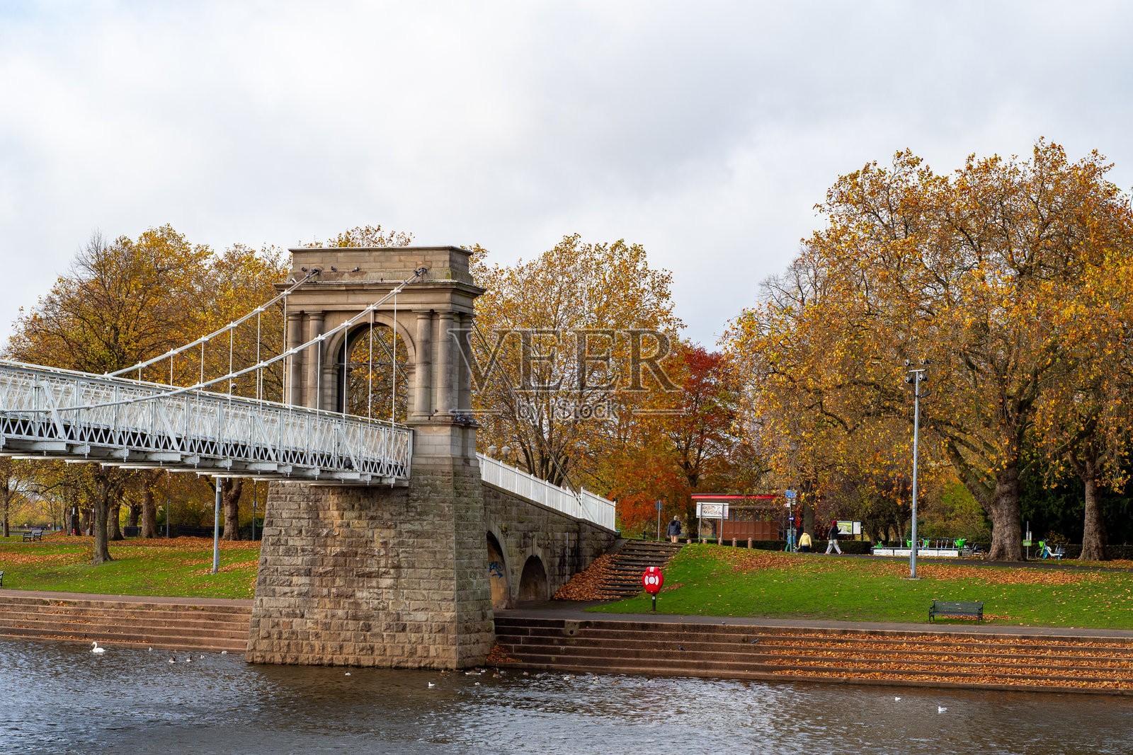 秋季色彩的树木环绕着横跨河流的悬索桥的景观视图。照片摄影图片