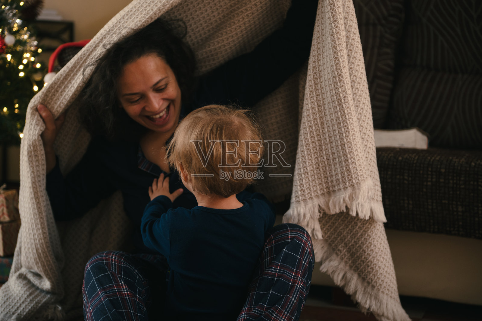 圣诞树旁，一位快乐的母亲和孩子在舒适的毯子下玩耍照片摄影图片