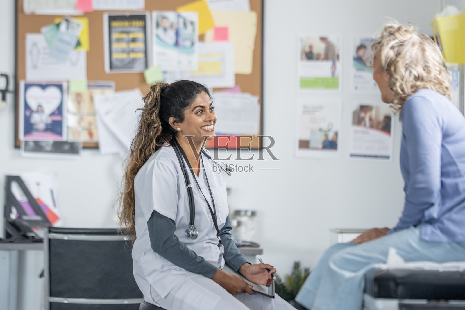 今日，一位南亚护士在医疗诊所微笑着与一位年长的白人患者进行友好互动。照片摄影图片