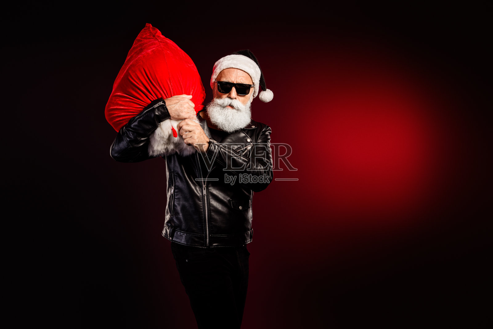 身穿皮夹克的摇滚风圣诞老人，背着巨大的红色礼物袋，置身于节日气氛浓厚的场景中，非常适合圣诞宣传和新年促销活动。照片摄影图片