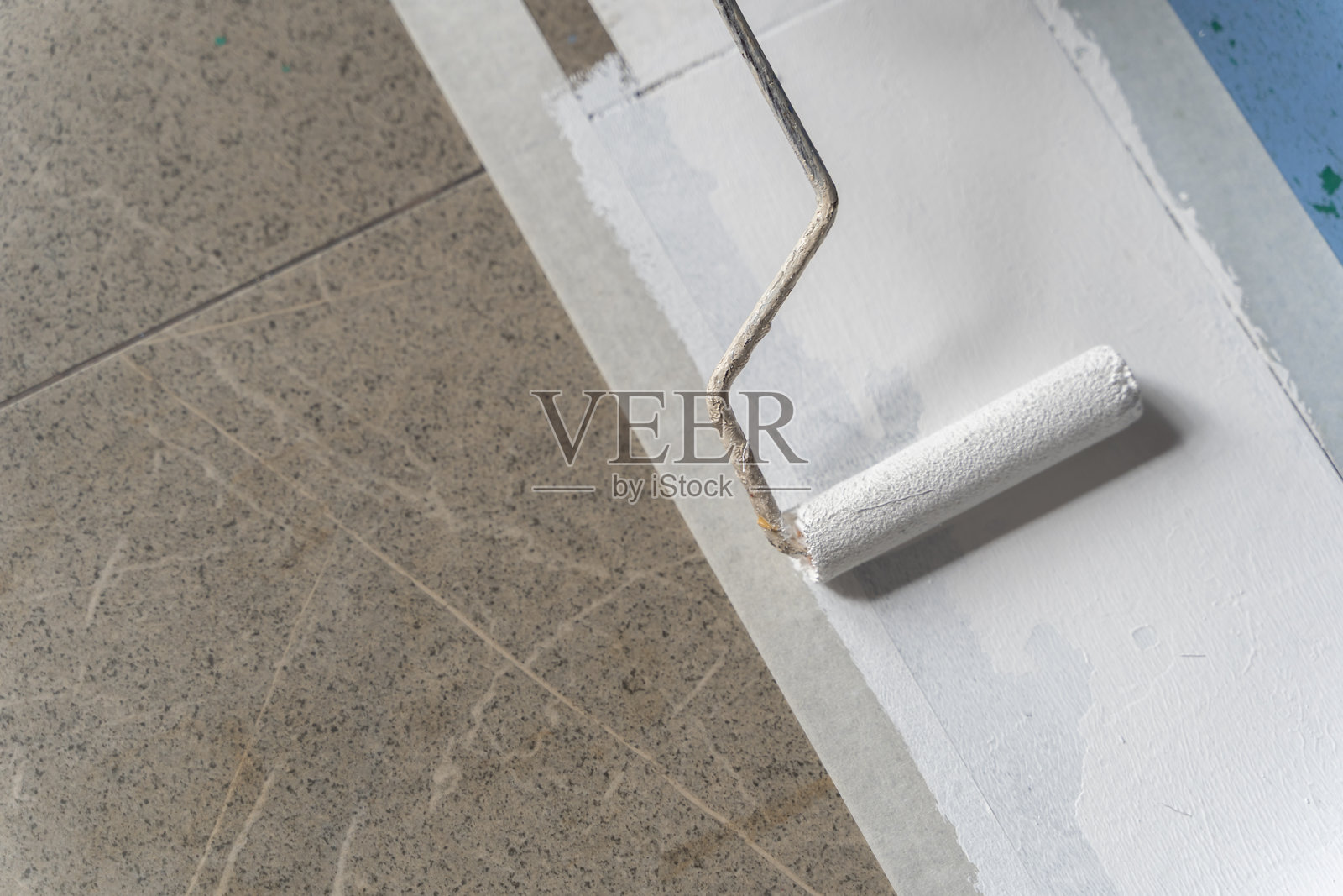 粉刷滚筒在地板边缘涂刷白色，并贴有遮蔽胶带，用于翻新和家居装修概念照片摄影图片