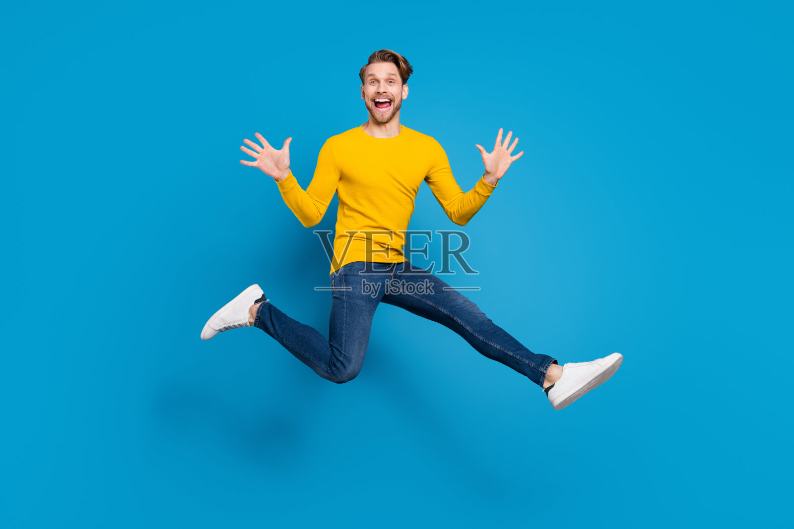 一个年轻男子全身照，他高高跃起，开怀大笑，背景是鲜艳的蓝色，充满喜悦照片摄影图片