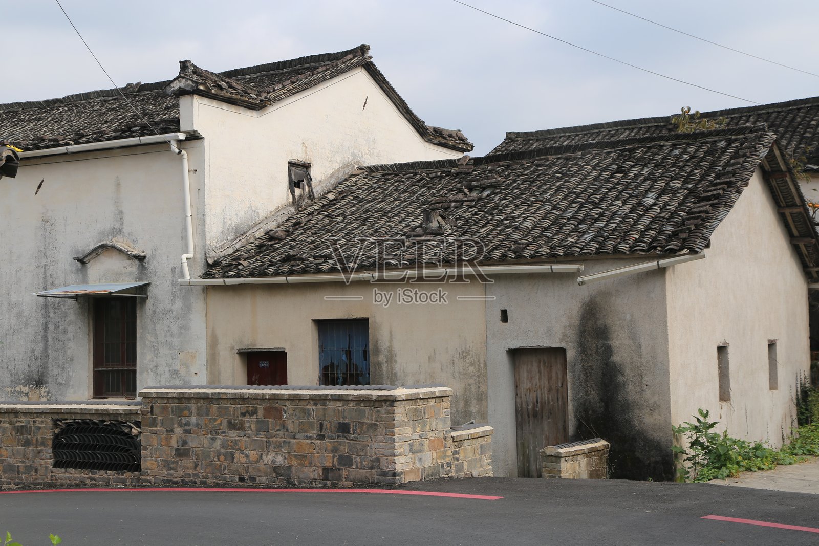 中国乡村一栋老房子，墙体简洁，屋顶铺有瓦片，外墙刷有白漆，下方露出石砖。照片摄影图片