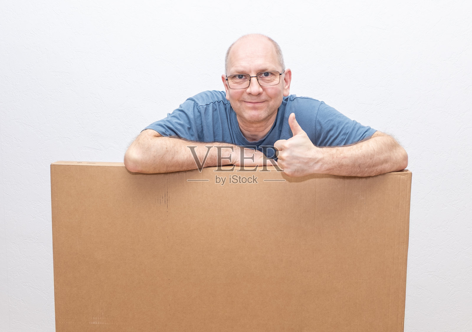 一个高加索男人靠着一个大纸箱，做出“酷”的手势。留有文字空间。照片摄影图片
