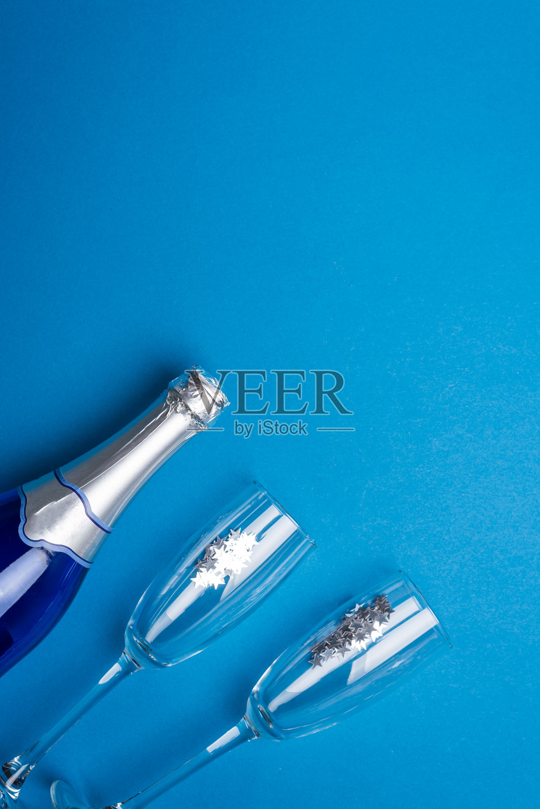 蓝色背景上带有银色装饰的香槟酒瓶和酒杯，用于新年庆祝照片摄影图片