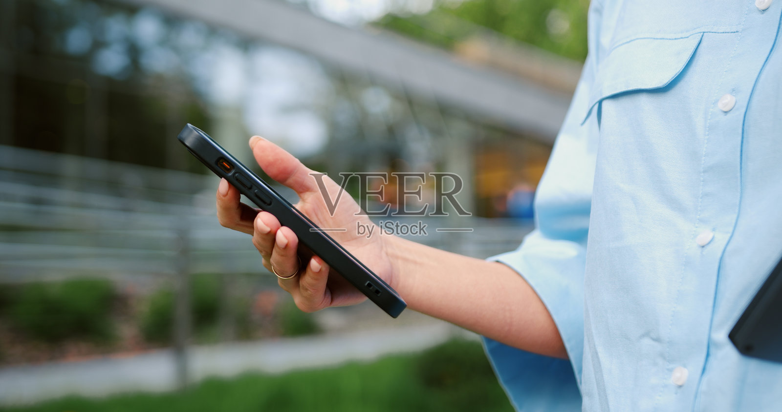 特写：一名女性的手在户外滑动智能手机屏幕，浏览信息或发送短信，展示了移动技术和数字通信的日常使用。照片摄影图片