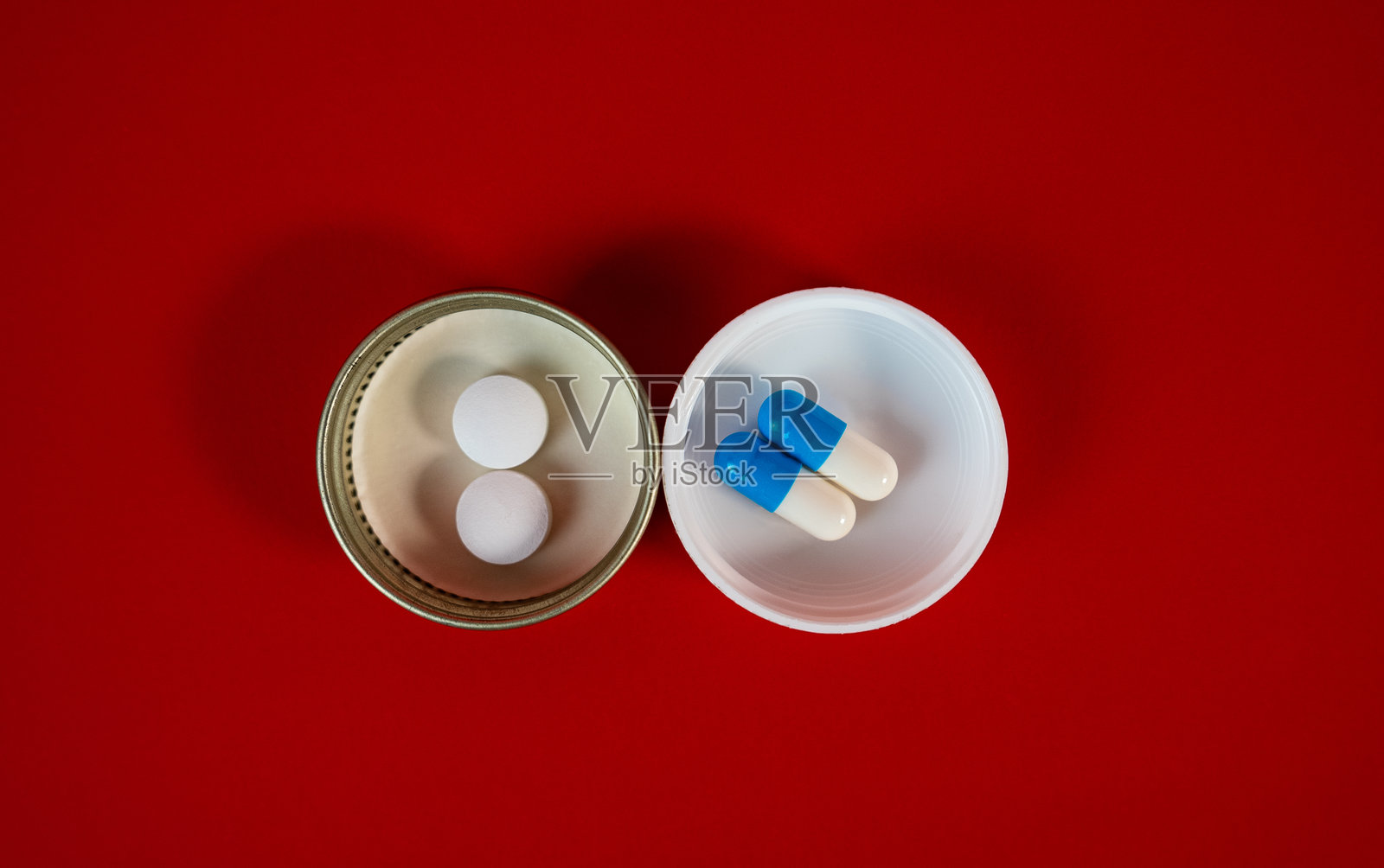 药片和蓝色胶囊对的两个瓶盖，红色背景俯视照片摄影图片