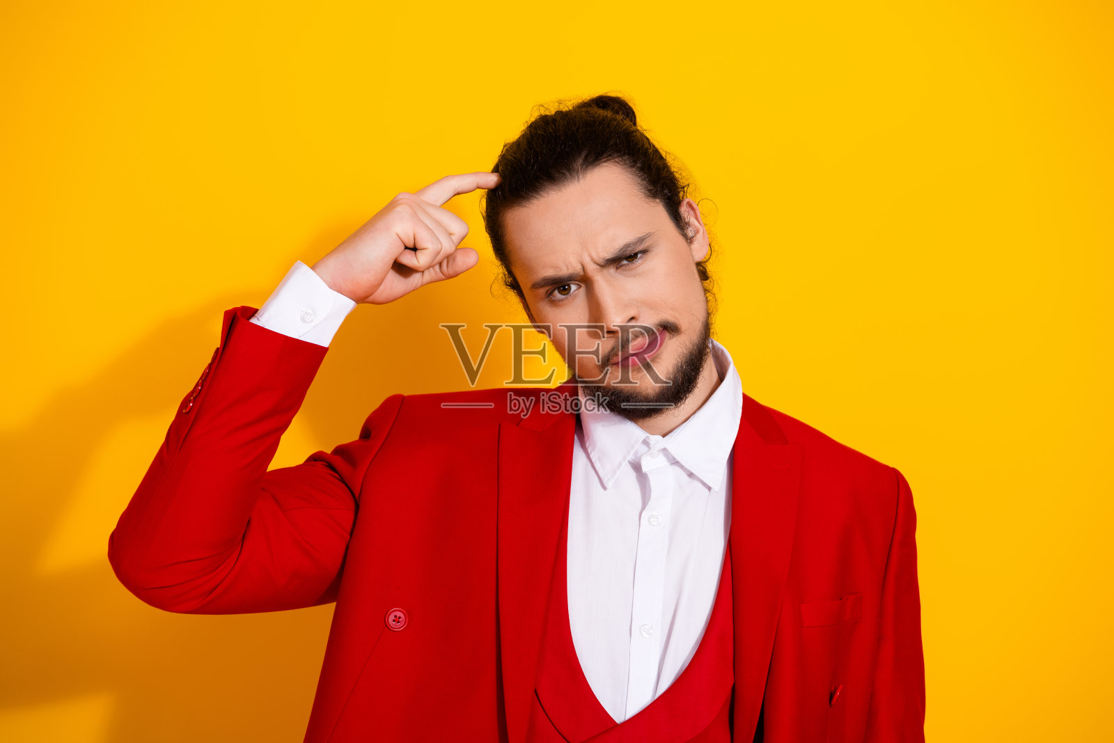 有趣的时尚瞬间：一位穿着鲜红色西装的时尚男士，在阳光明媚的黄色背景前摆出困惑的姿势。照片摄影图片