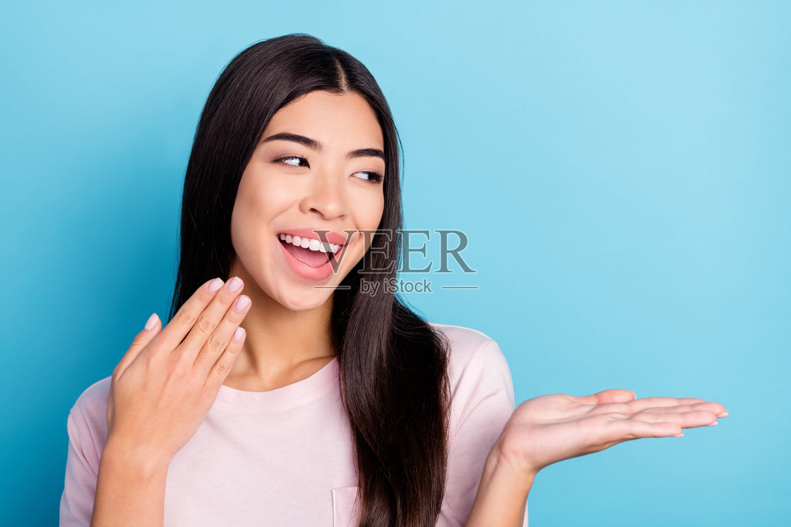 一位迷人的、快乐的、惊讶的女孩肖像，手掌托着空白的复制空间用于广告宣传，背景是明亮的蓝色照片摄影图片