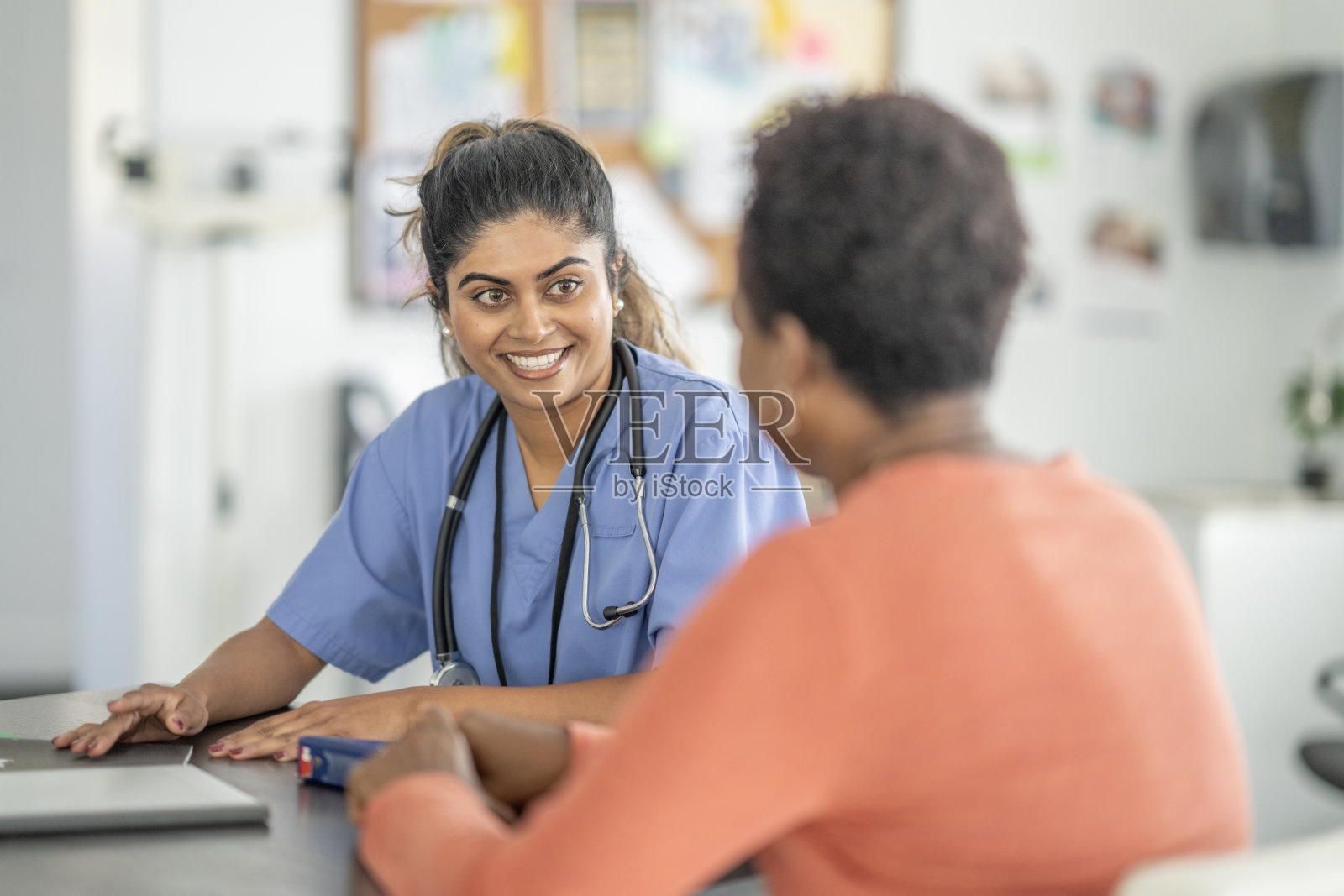 友好的南亚护士穿着蓝色工作服在诊所与非洲裔患者交谈照片摄影图片