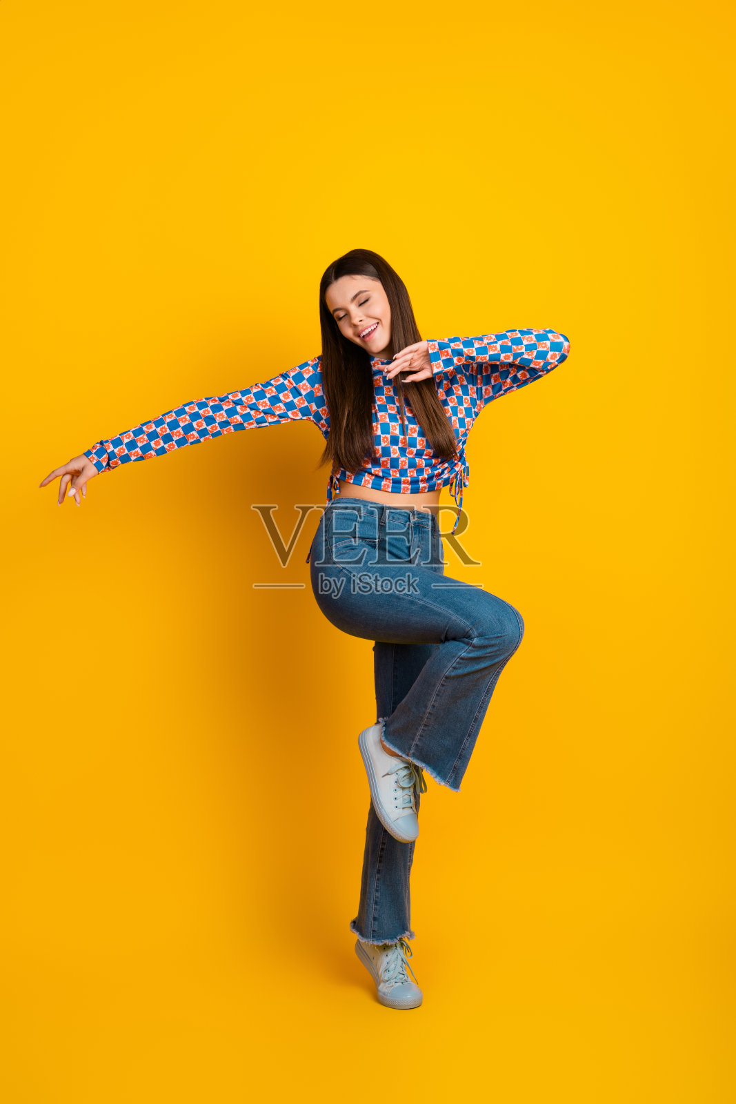 年轻女子穿着休闲时尚的服装，在明亮的黄色工作室里快乐地跳舞照片摄影图片