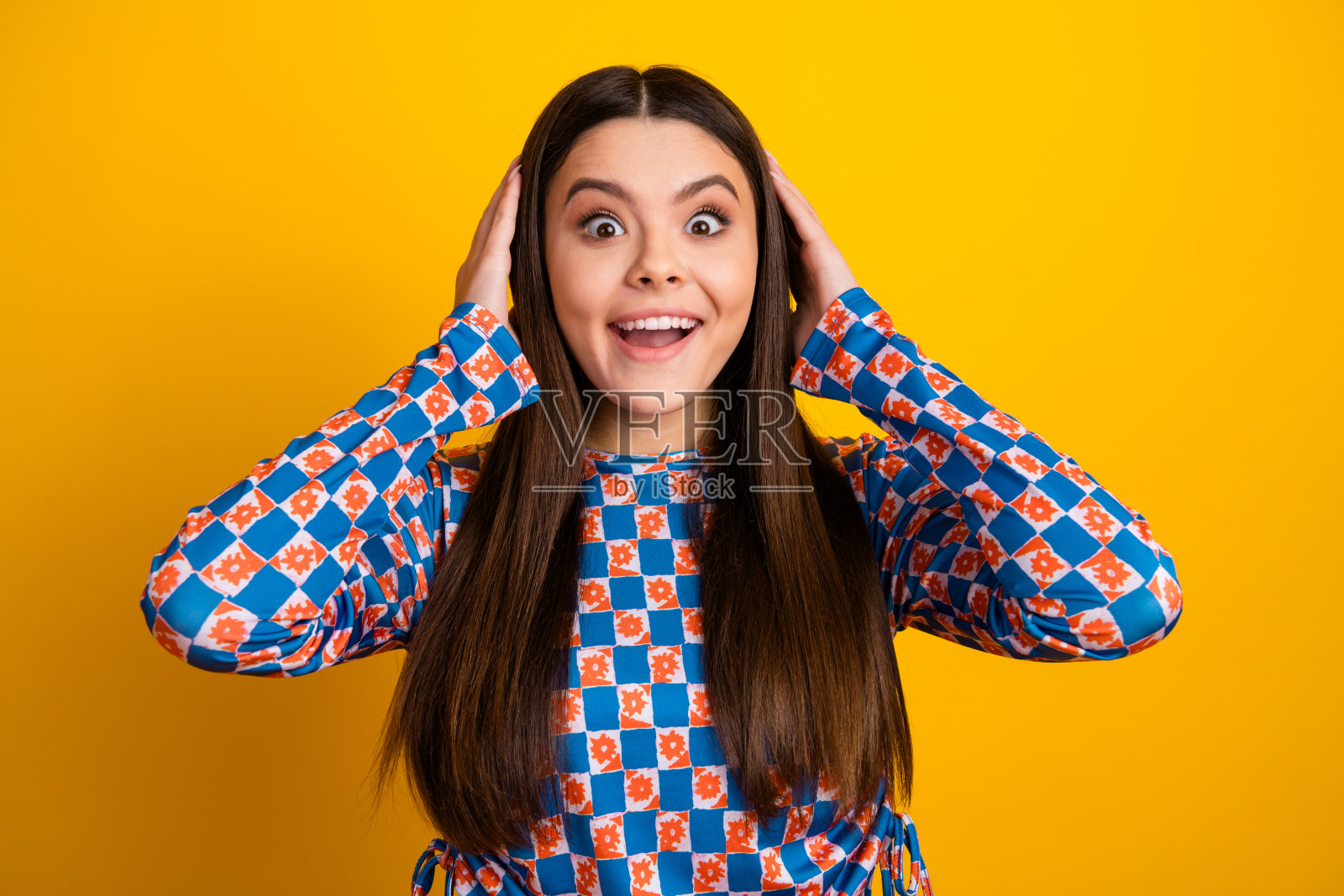 身穿大胆的蓝橙格纹连衣裙的快乐拉丁女孩，在明亮的黄色背景前微笑，用于时尚生活方式广告照片摄影图片