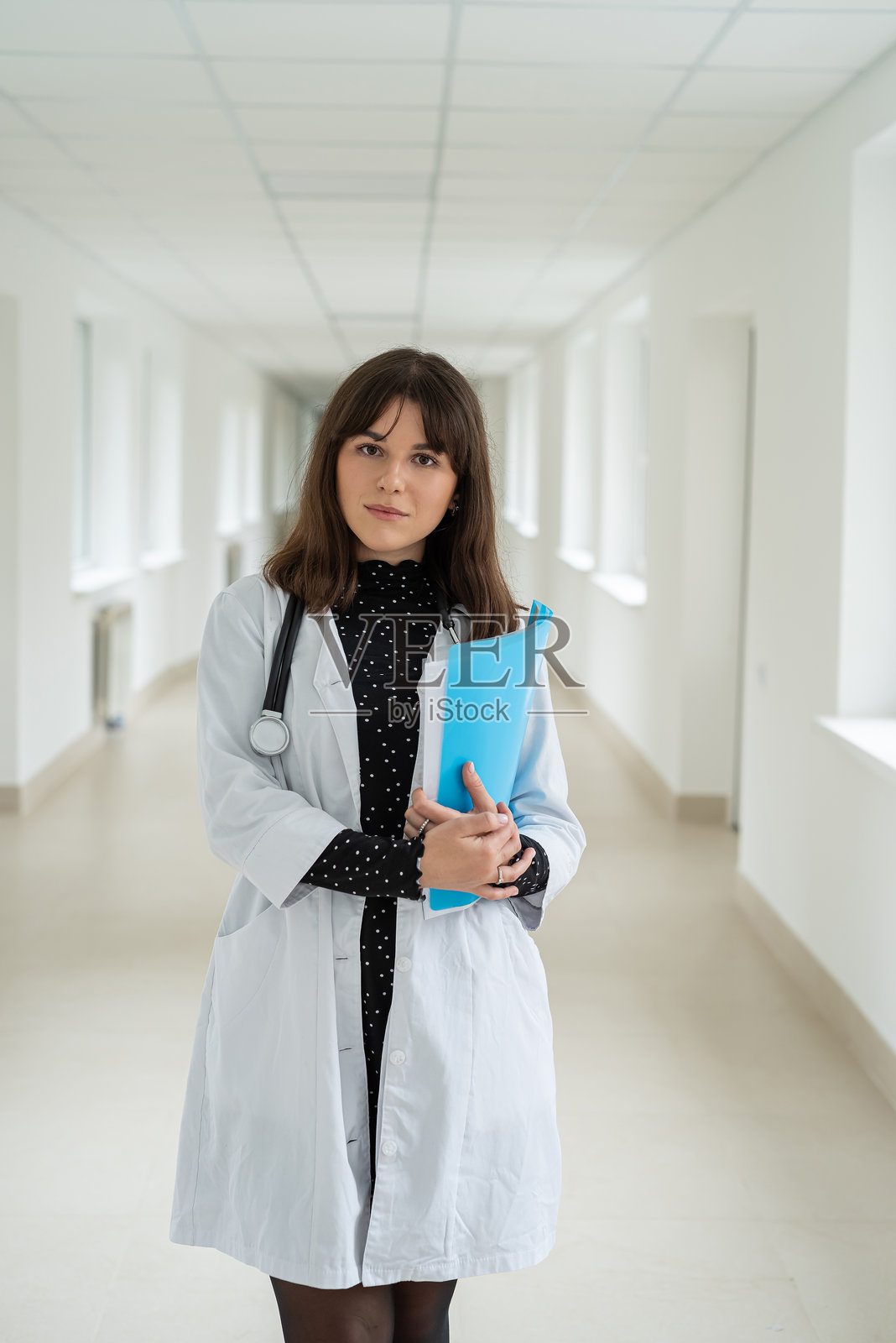 一名有魅力的白人女护士或女学生穿着制服，戴着听诊器，在诊所走廊里。照片摄影图片