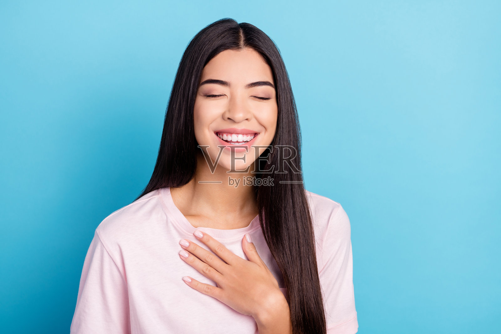 年轻女孩快乐积极的笑容，手放在胸前，开怀大笑，有趣的笑话，孤立在蓝色背景上照片摄影图片