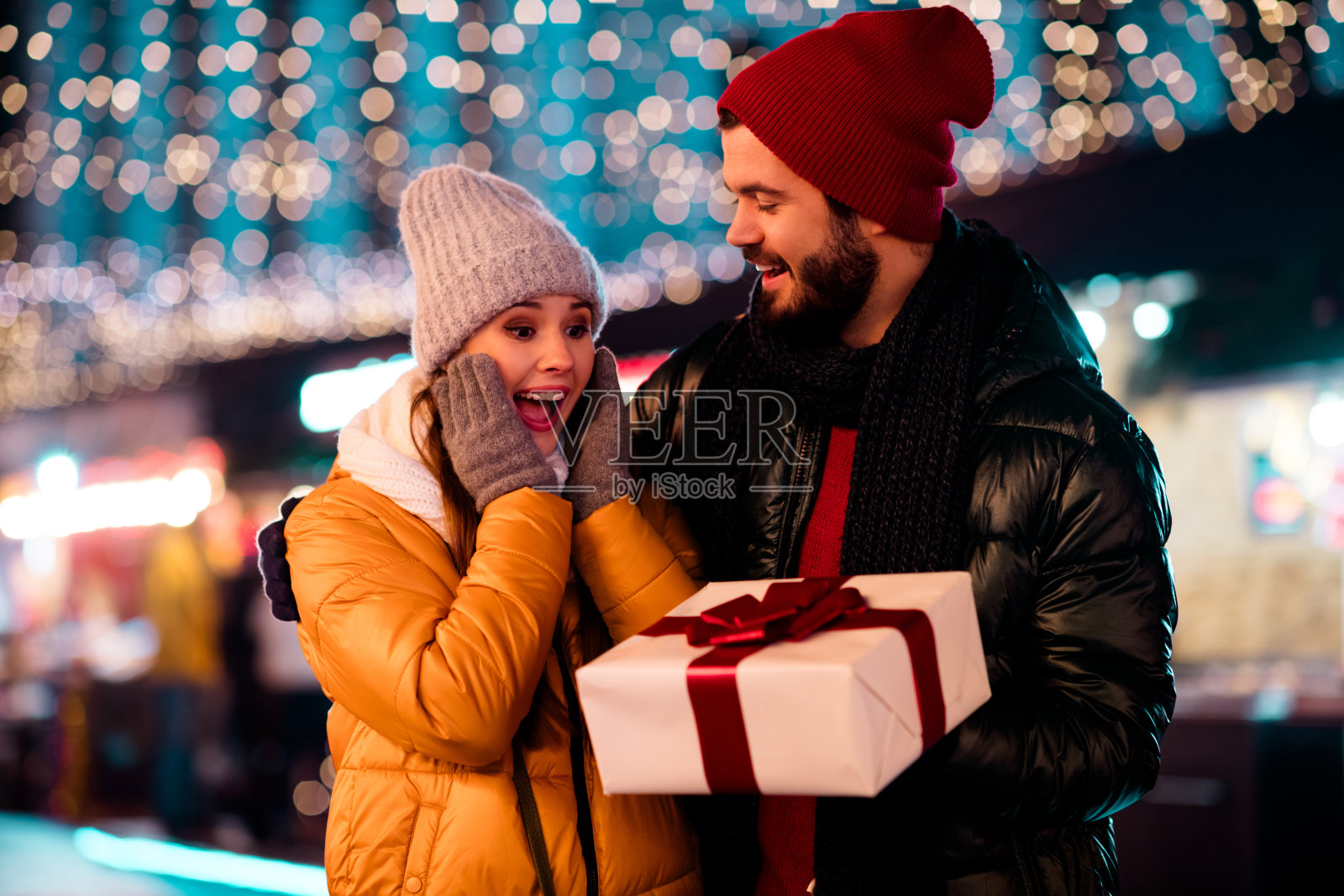 一对情侣在节日灯光下，惊喜地分享着圣诞礼物，开怀大笑，共庆圣诞喜悦照片摄影图片