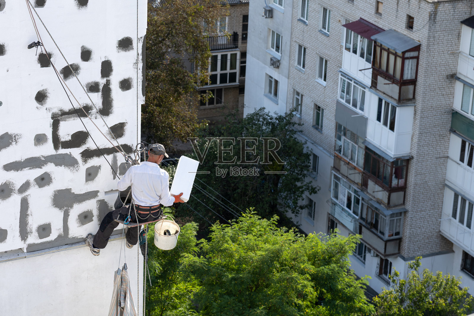 九层楼高的建筑外墙保温施工现场的建筑工人。照片摄影图片