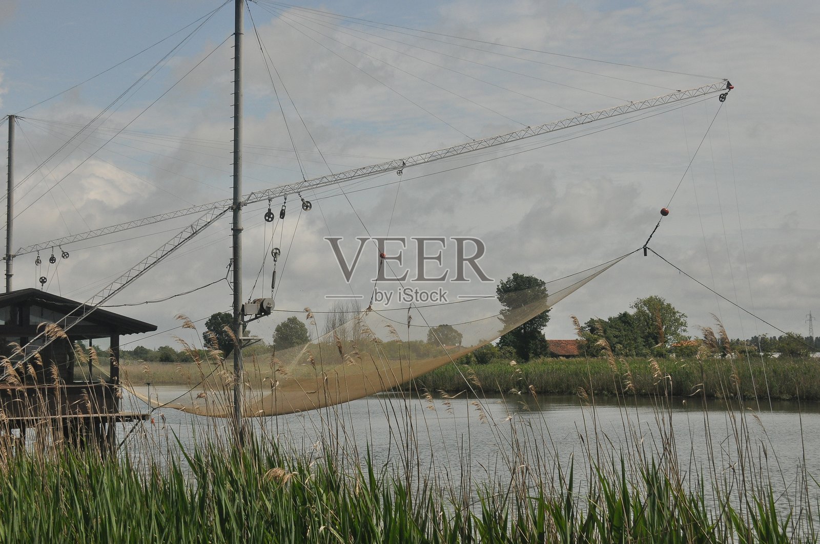 宁静的河景，背景是垂钓的渔网，点缀着绿植，远处有建筑，天空布满云彩照片摄影图片