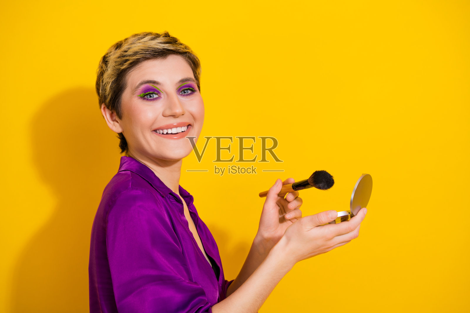 年轻女子在鲜艳的黄色背景前微笑，化着亮紫色眼妆，展现时尚魅力与风格照片摄影图片