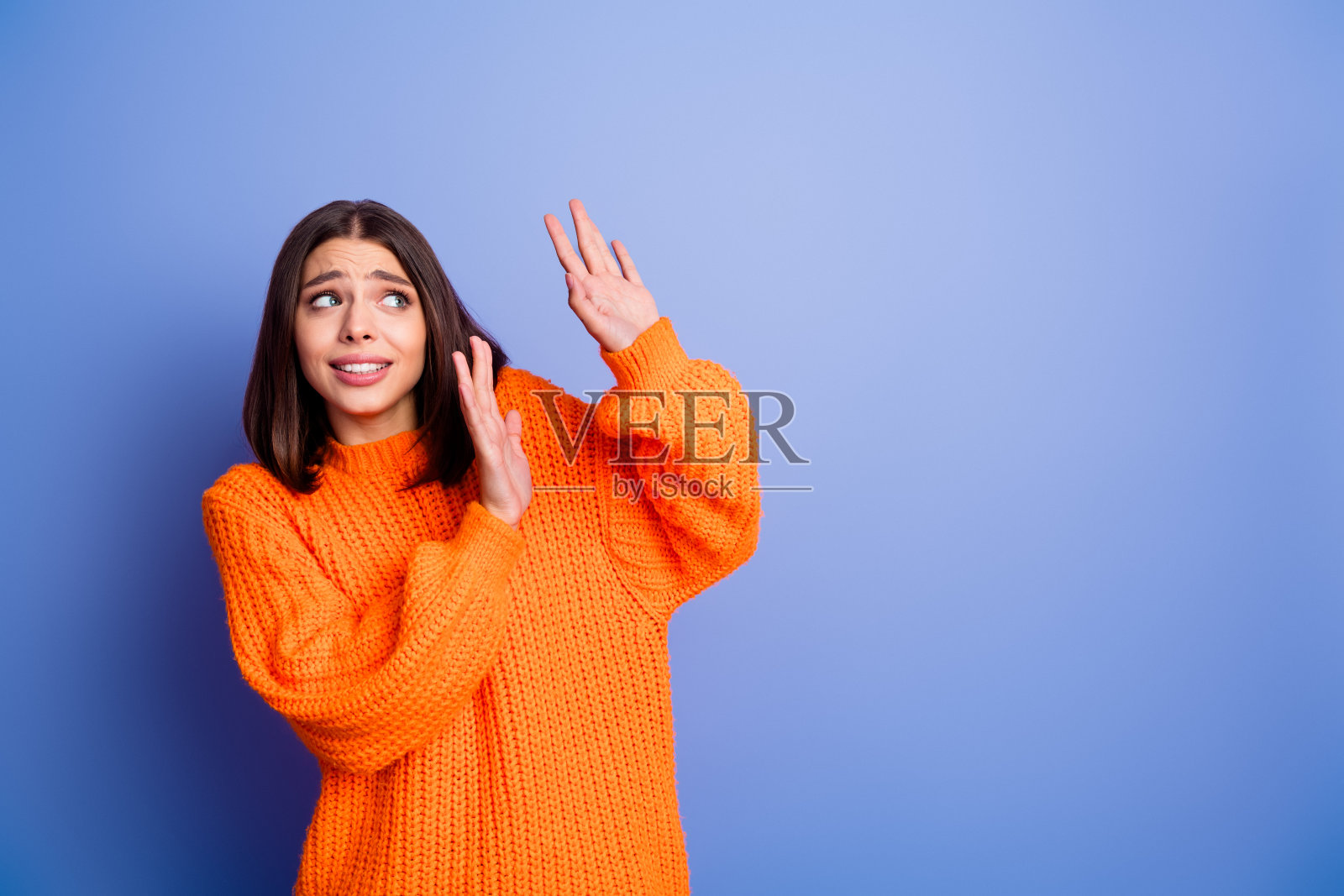 穿着橙色毛衣的年轻女子，在蓝色背景前露出惊讶的表情，传达出秋季的时尚风格。照片摄影图片