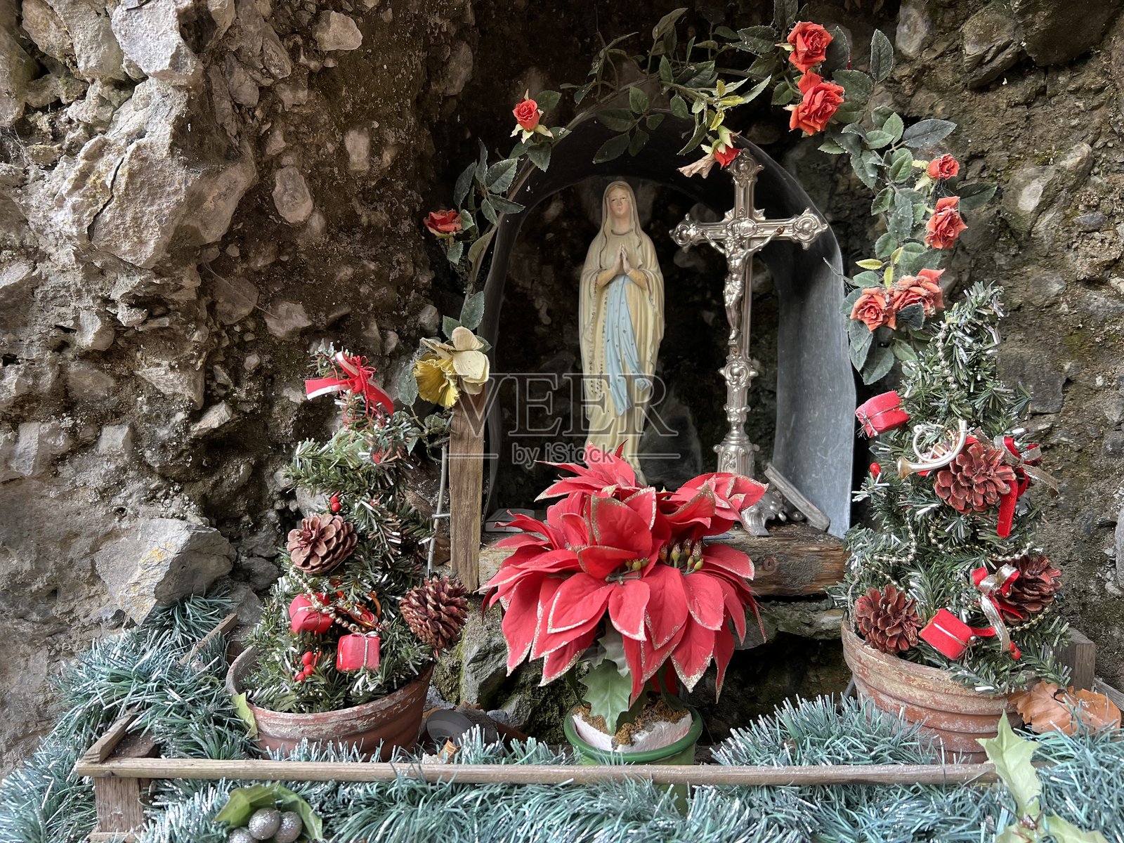 在瑞士上瓦尔登州恩格尔贝格的一座岩石雕刻小教堂里，圣母玛利亚手捧节日圣诞花卉布置，教堂外观宛如洞穴。照片摄影图片