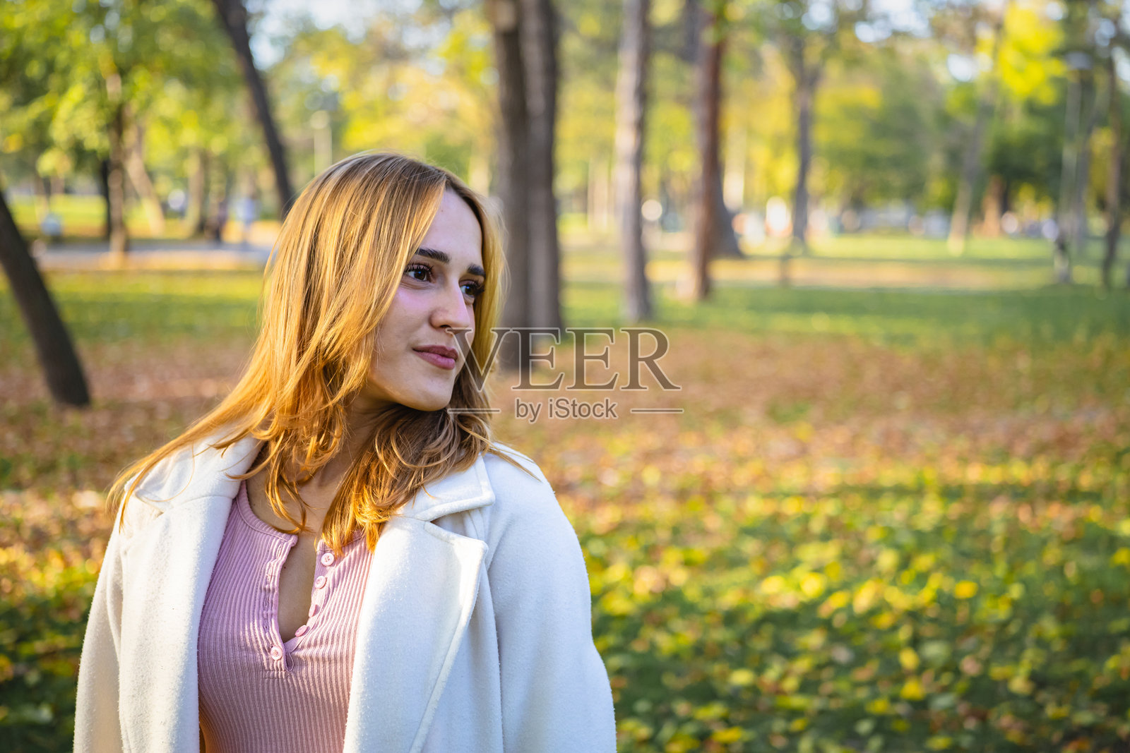 一位美丽的年轻女子在公园里散步，享受着落满秋叶的美丽秋日时光。照片摄影图片