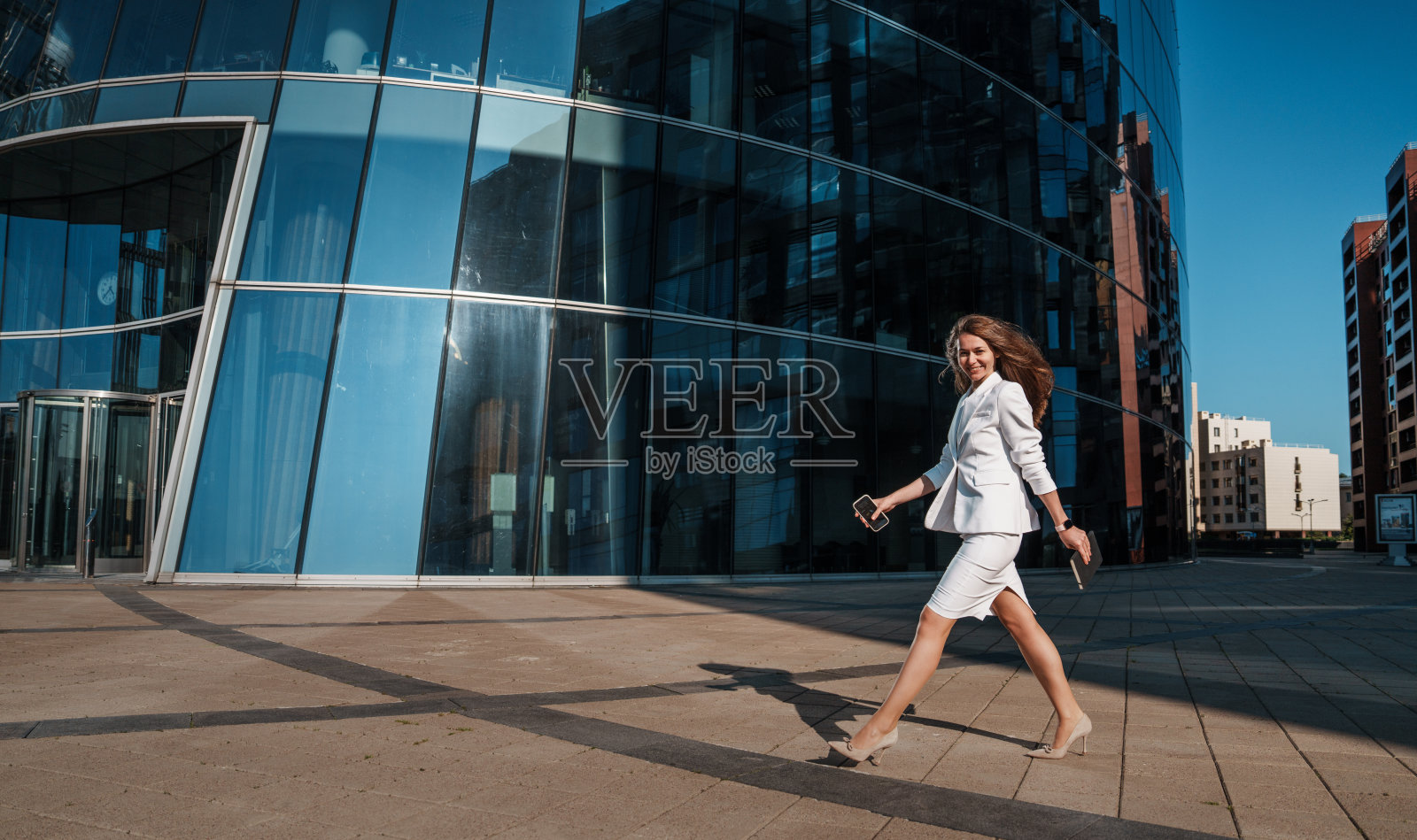 一位身着合身服装的微笑女士，悠闲地倚靠在石阶旁的栏杆上，在城市环境中散发着优雅与放松的气息。照片摄影图片