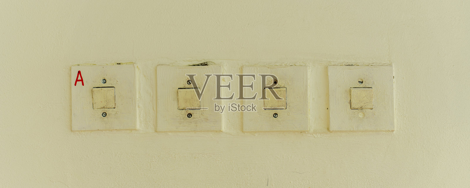 奶油色墙壁上并排安装的四个老式电灯开关，其中一个开关标有A，显示出年代感和磨损痕迹照片摄影图片