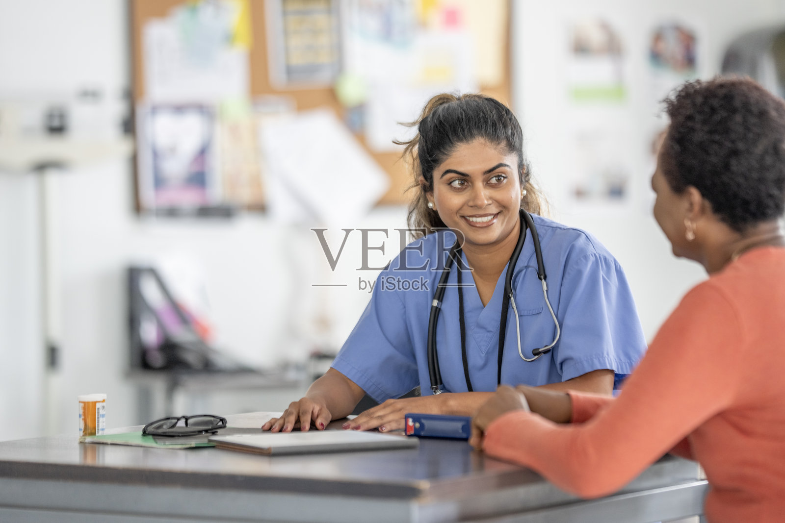 穿着工作服的亚裔护士在诊所接待处与病人交谈照片摄影图片