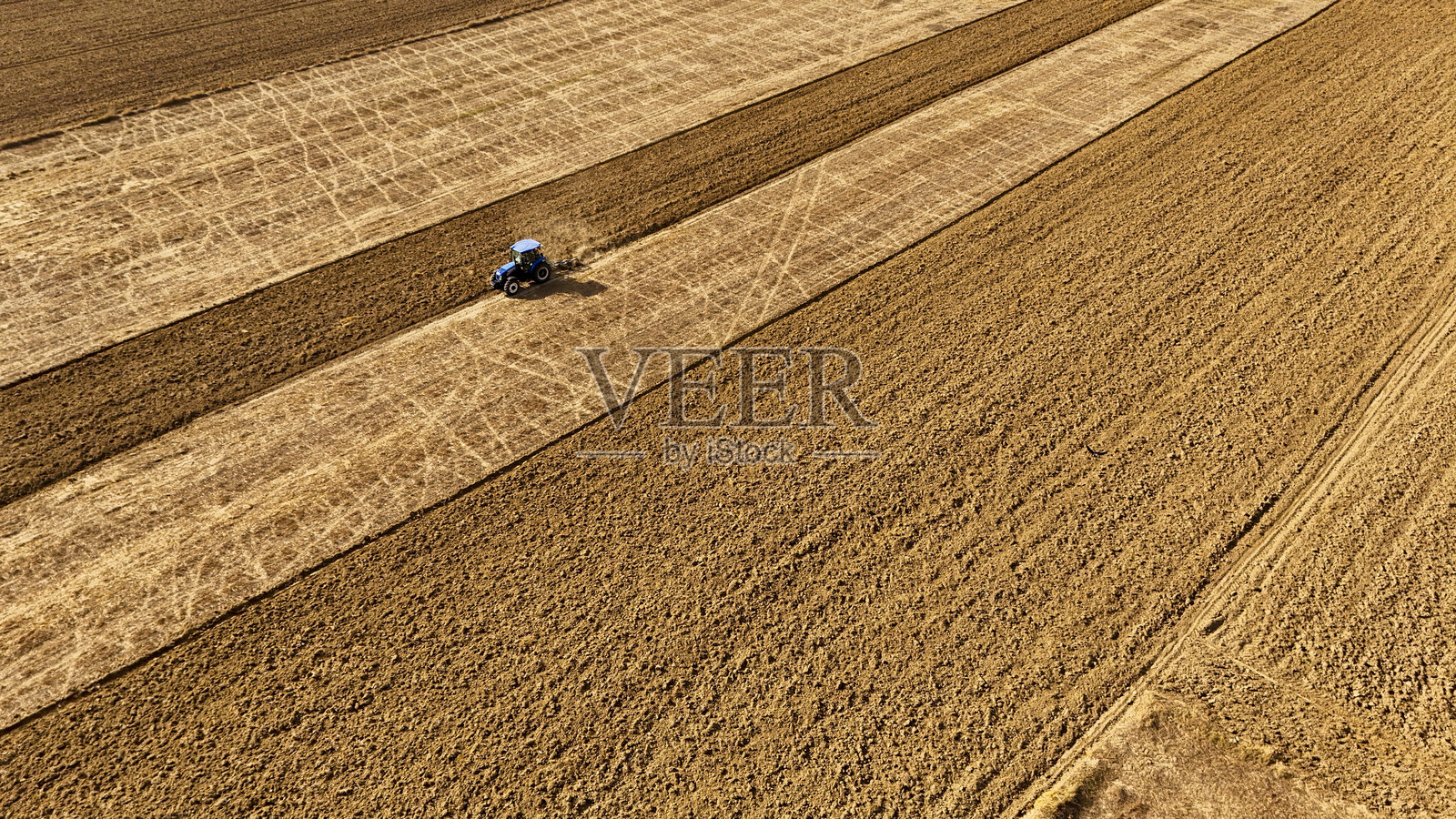 航拍无人机镜头，在阳光明媚的日子里，广阔的田野中拖拉机正在耕作土壤照片摄影图片