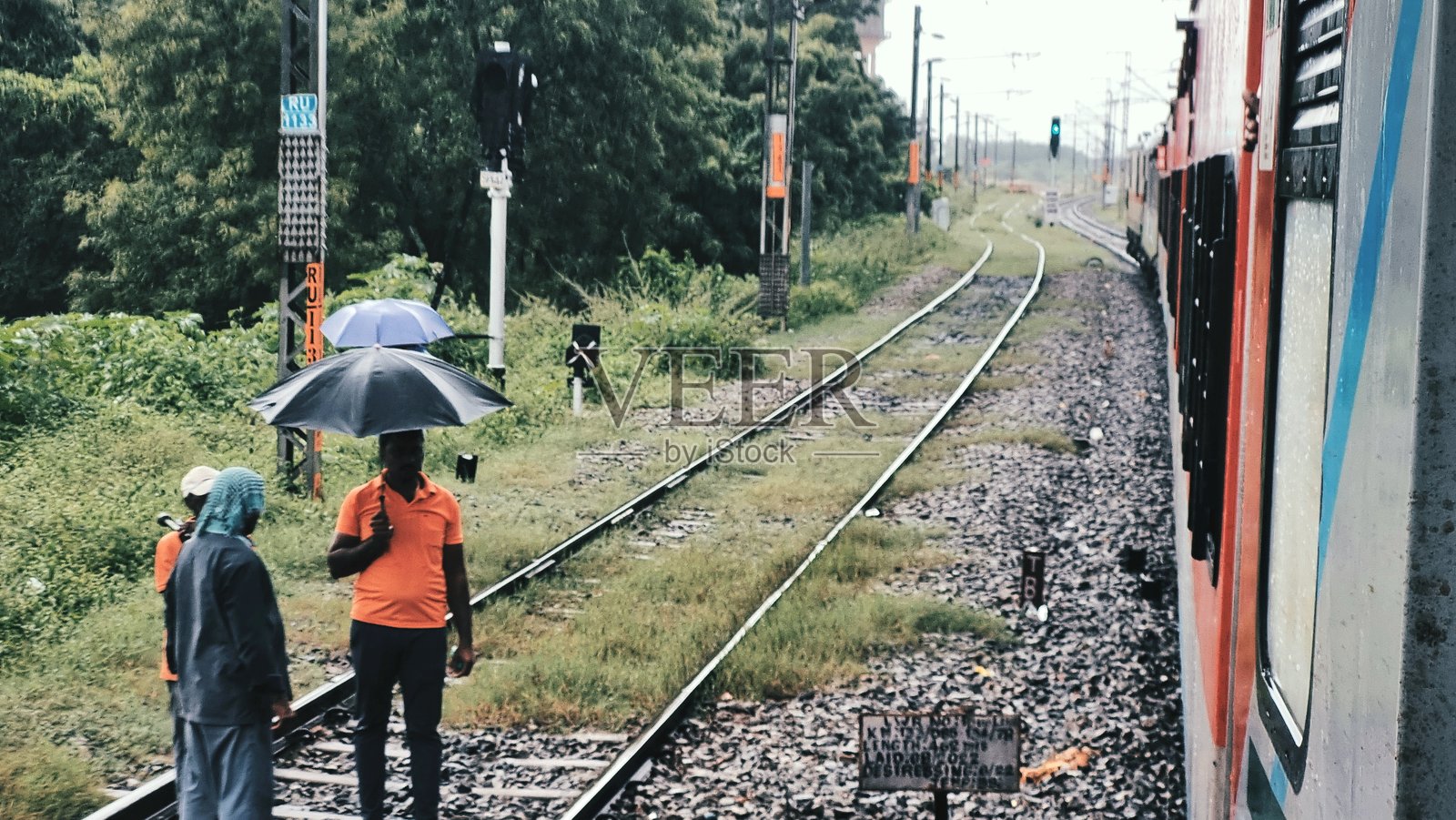 印度铁路穿过茂密的乡村，一位铁路工程师雨中打着伞检查轨道照片摄影图片