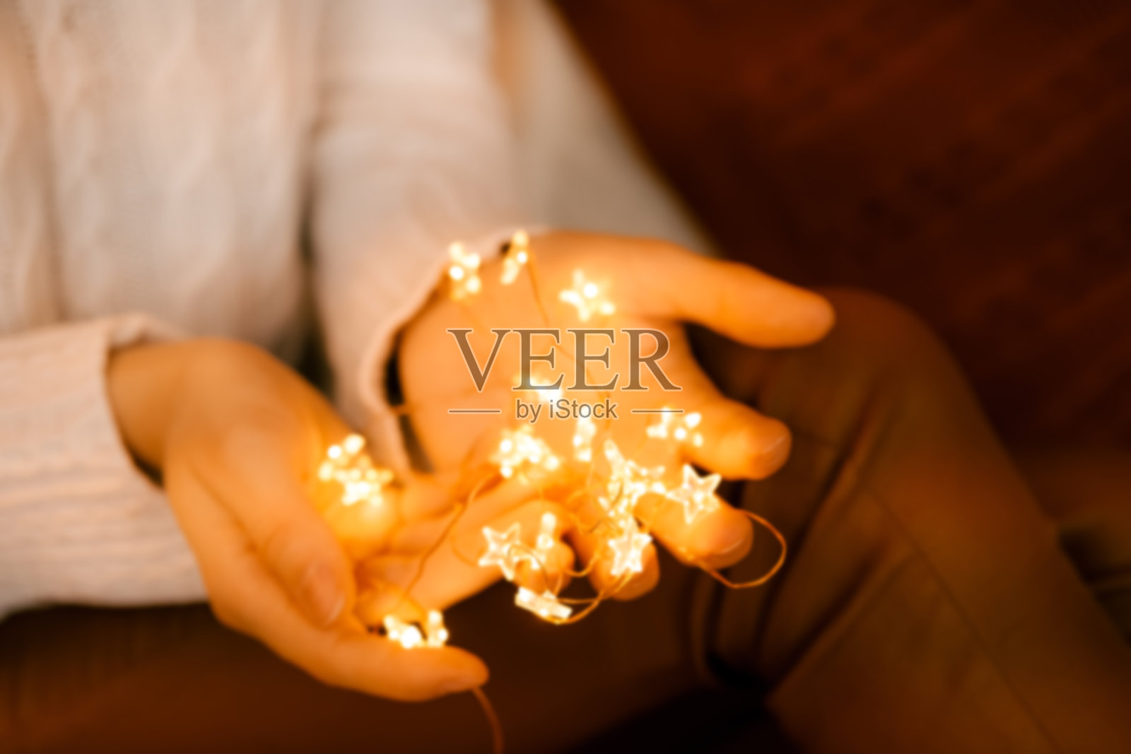 一个穿着白色毛衣的女孩手里拿着星光花环。新年氛围，期待节日，许愿照片摄影图片