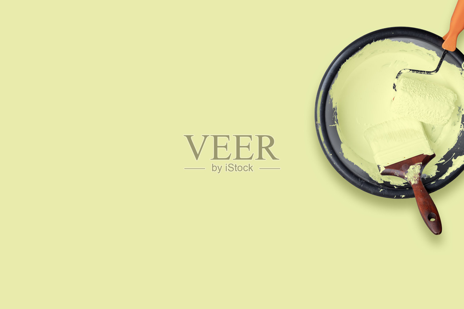 用于家居装修概念的托盘中带有粉彩黄颜料的油漆滚筒和画笔俯视图，背景为粉彩黄照片摄影图片