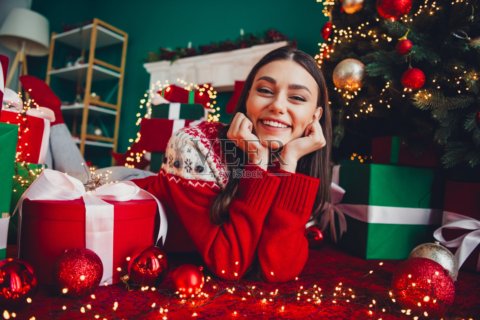 温馨的圣诞时光，一个小女孩依偎在闪烁的圣诞树旁，树上挂满了礼物和舒适的节日灯饰，室内场景。照片摄影图片