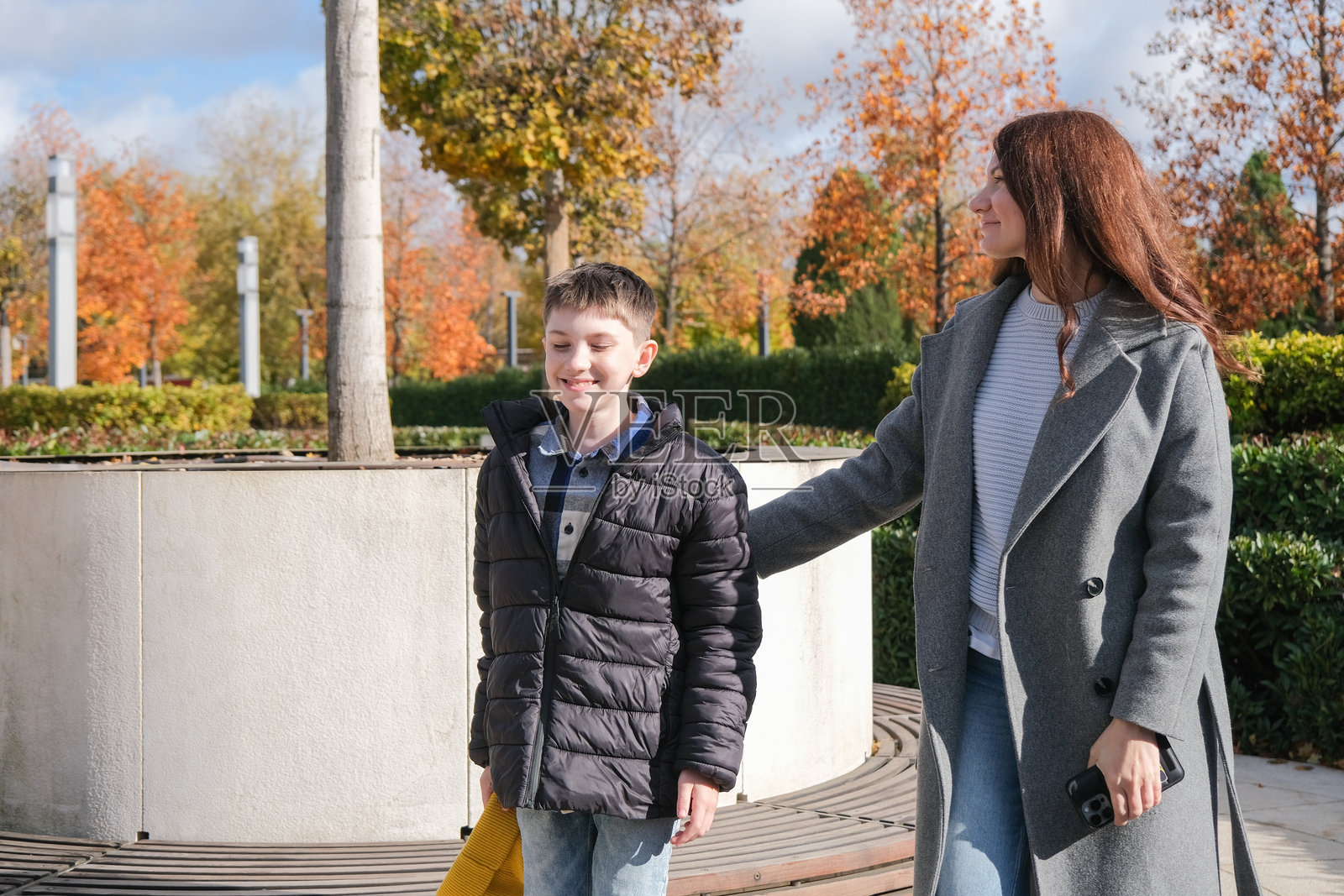 男孩和他的母亲站在公园长椅附近交谈照片摄影图片
