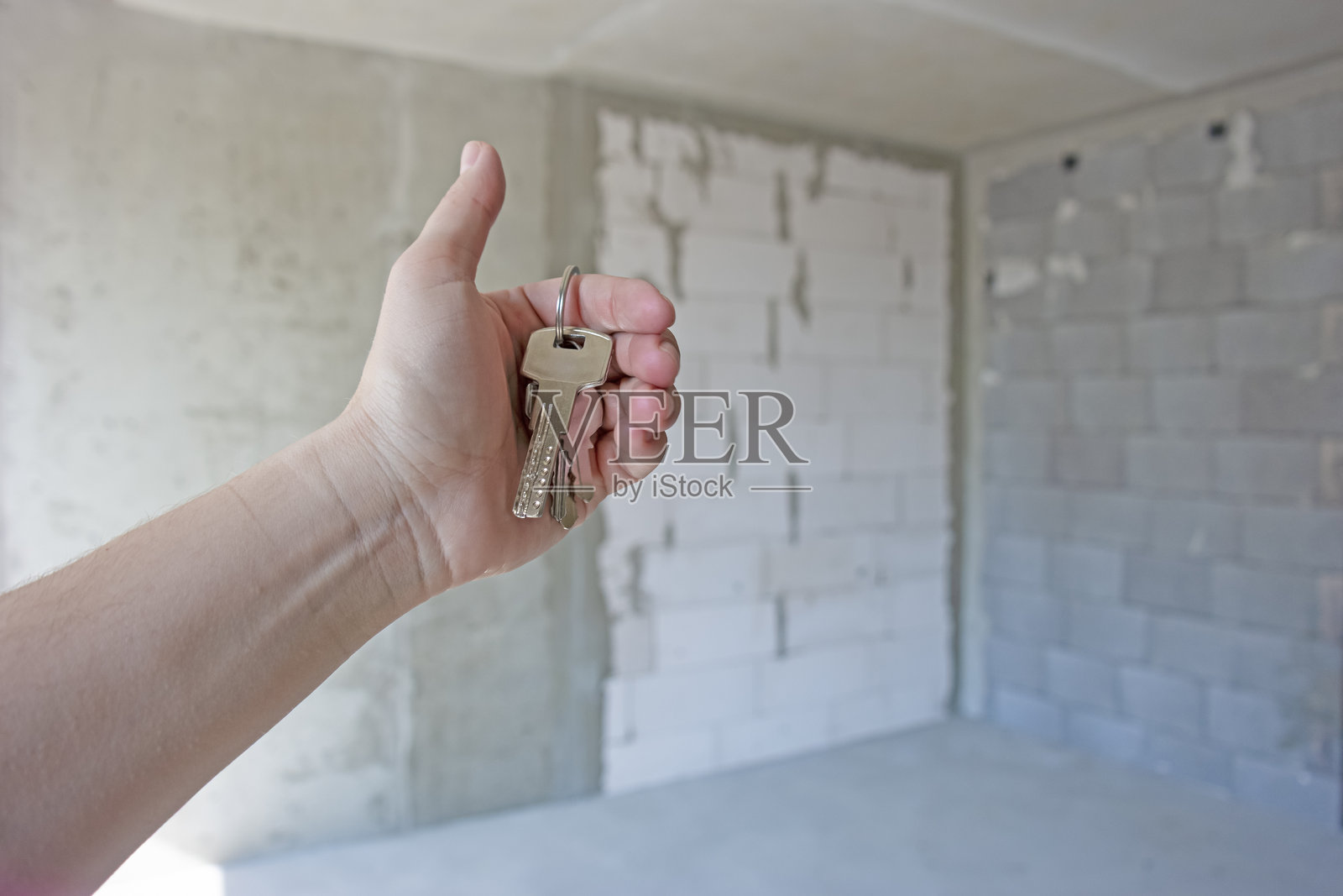 房地产概念。一位女士的手握着钥匙，在手指上展示，背景是正在粗略装修的新公寓楼。照片摄影图片