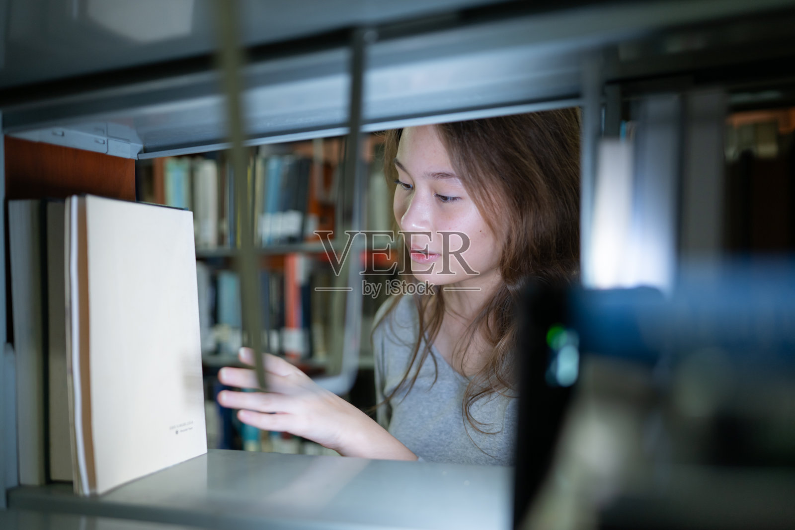 一个十几岁的女孩站在图书馆的书架之间照片摄影图片