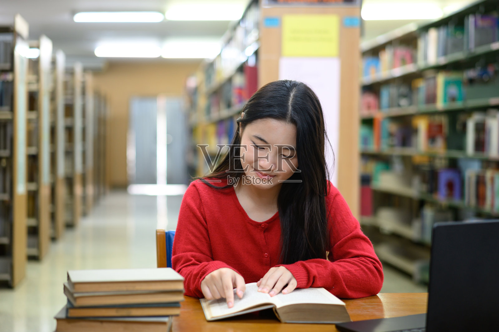亚洲少女在图书馆学习区专注而微笑地阅读照片摄影图片