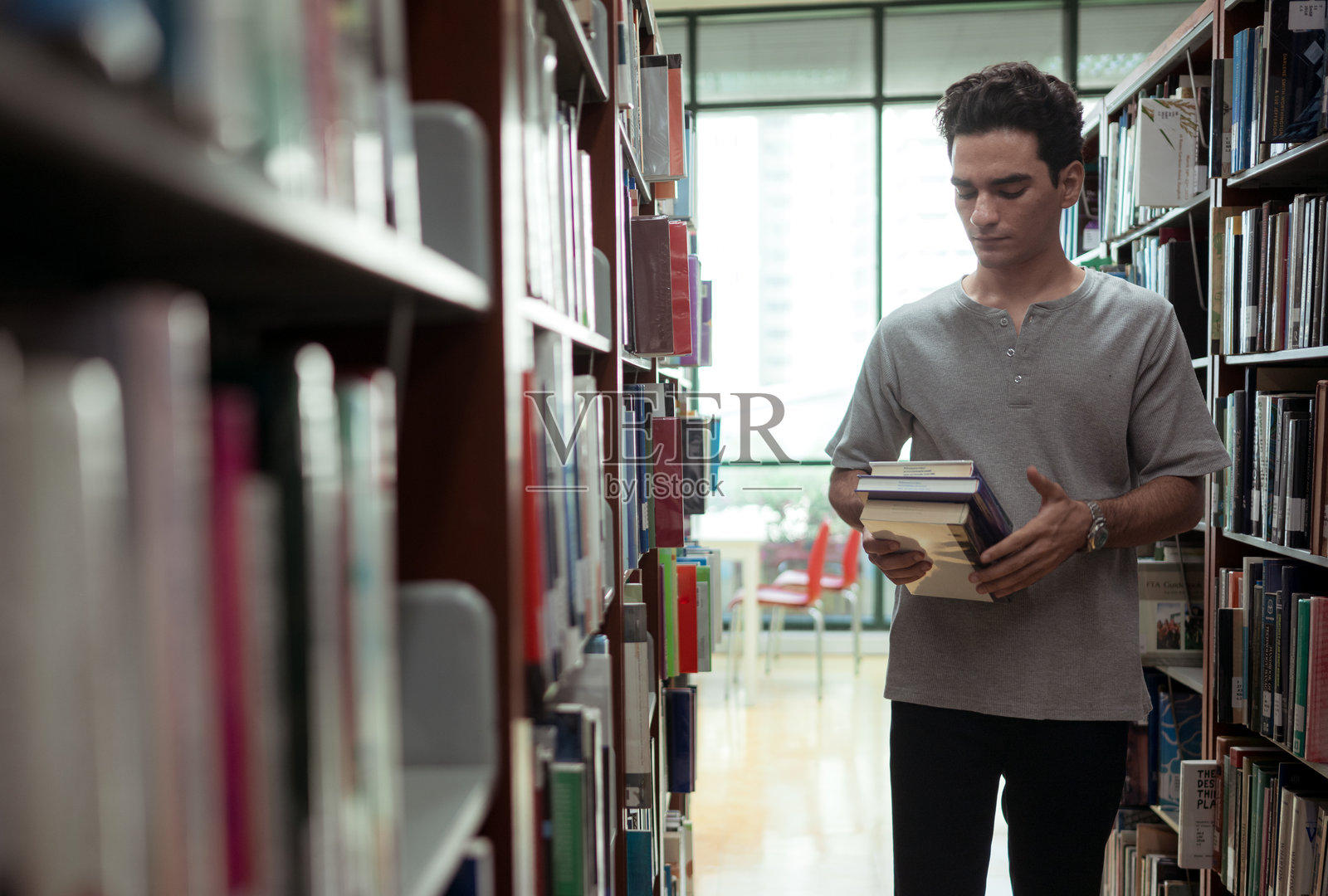 一个年轻男子站在图书馆的书架之间照片摄影图片