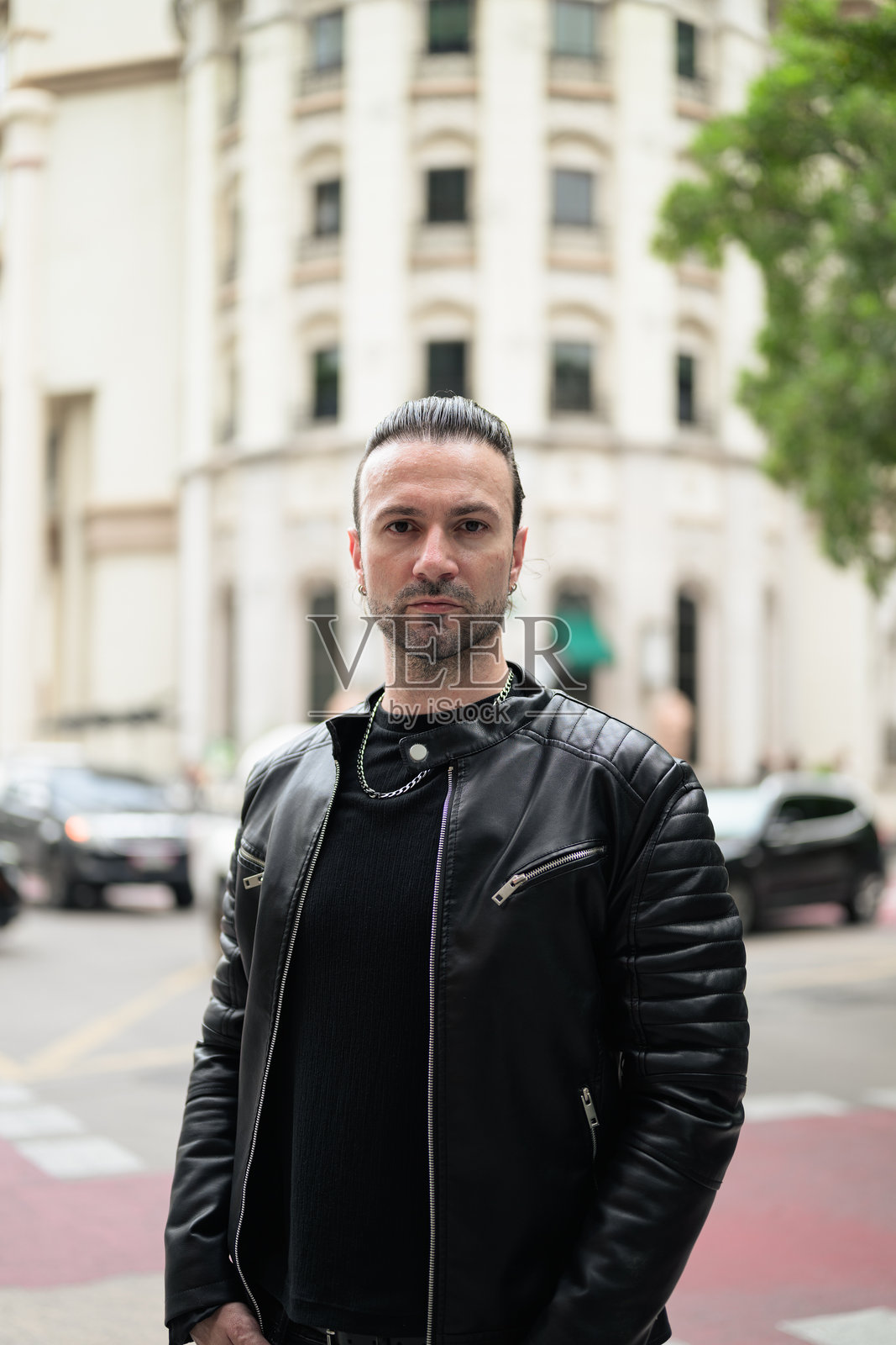 英俊的络腮胡男子身穿黑色皮夹克，在城市街道上摆姿势。照片摄影图片