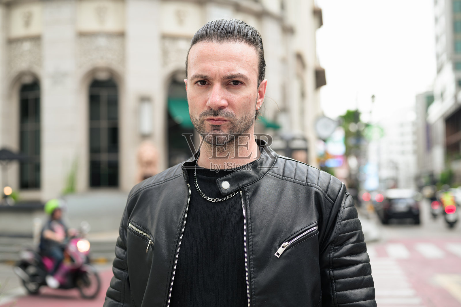 英俊的胡子男人穿着黑色皮夹克，在城市街道上摆姿势照片摄影图片