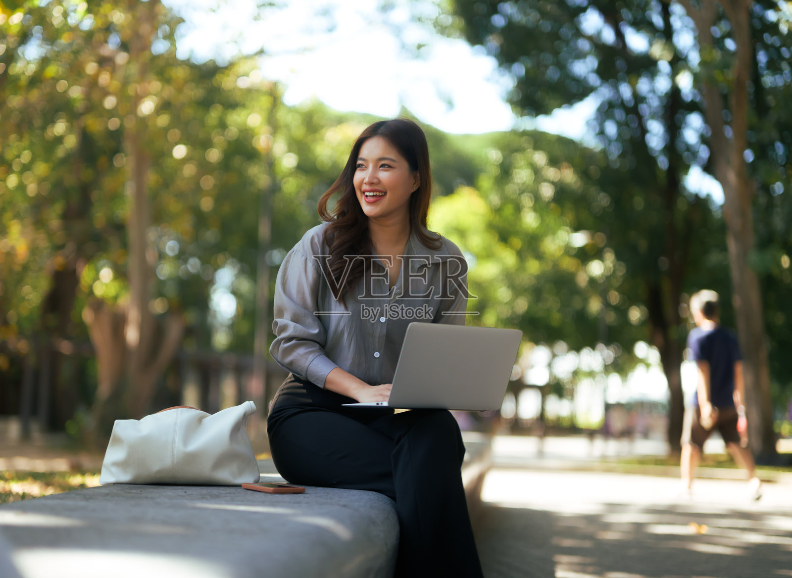 年轻女子在公园里享受远程工作，在轻松的环境中微笑着使用笔记本电脑。照片摄影图片