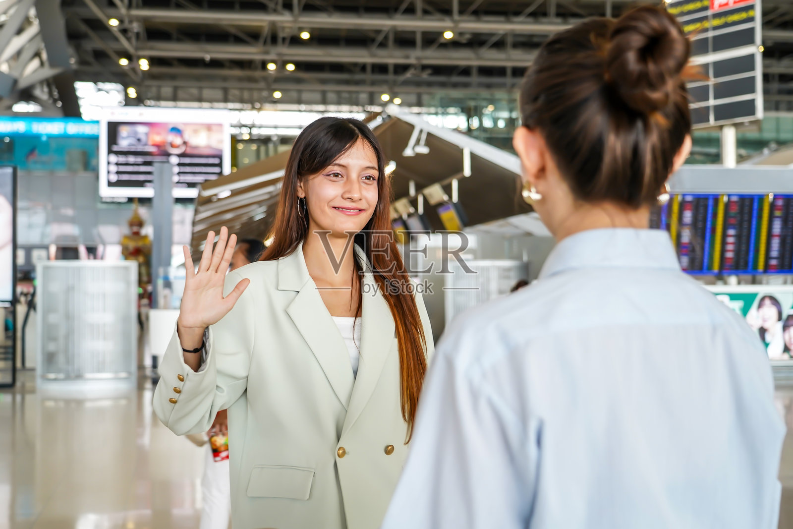 两位年轻亚洲女性在机场进行着温馨的对话，在告别时分享着欢笑和泪水，在踏上各自旅程前紧紧拥抱。照片摄影图片
