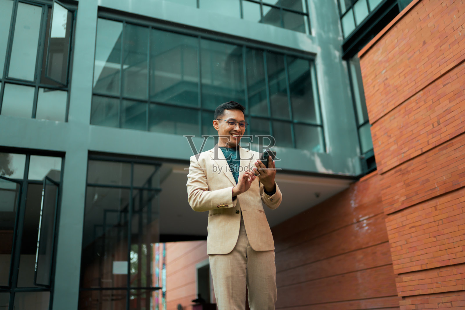 年轻商务男士在城市环境中，面带微笑，站立并使用智能手机。照片摄影图片